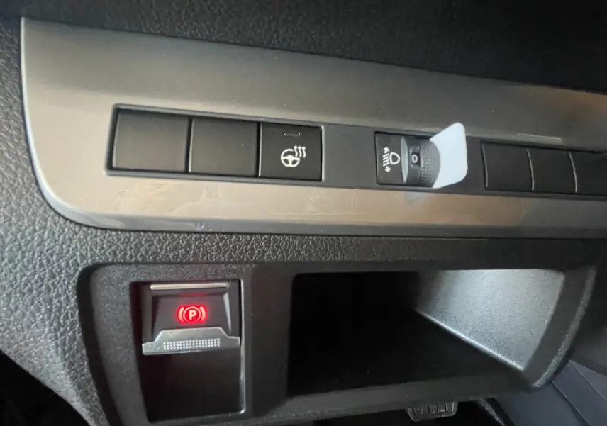 Gros plan sur les commandes intérieures du Peugeot Traveller noir 2026, avec bouton frein à main électronique allumé en rouge.