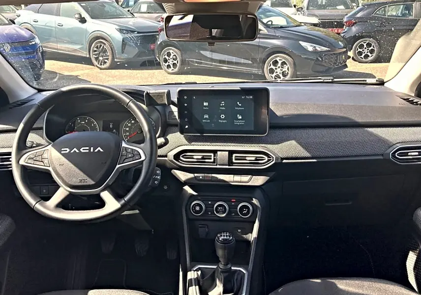 Vue intérieure avant de la Dacia Sandero 2025, tableau de bord noir avec écran tactile et volant multifonctions.