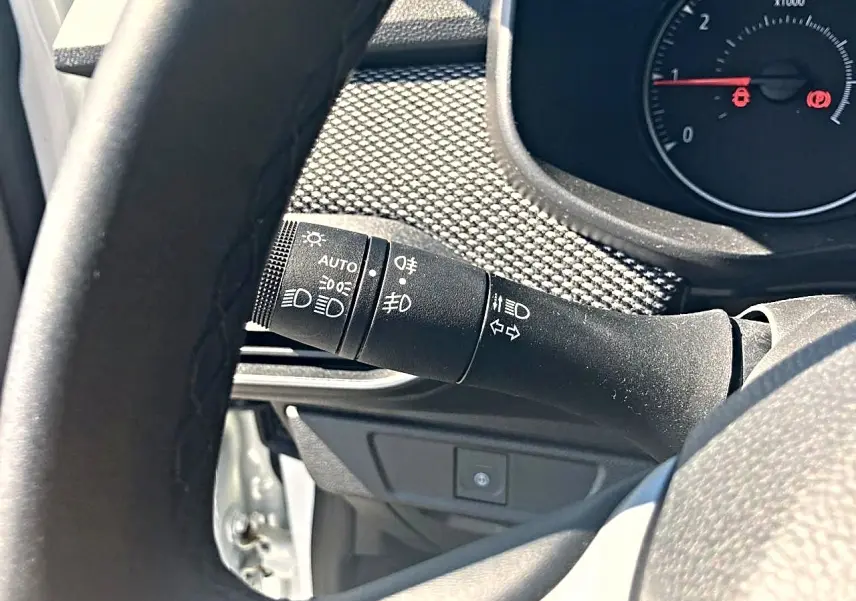 Gros plan sur la commande des phares et clignotants côté gauche du tableau de bord d’une Dacia Sandero blanche 2025.