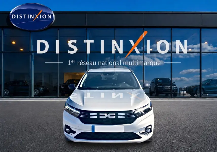 Vue frontale d'une Dacia Sandero blanche 2025 garée devant une vitrine avec logo Distinxion.