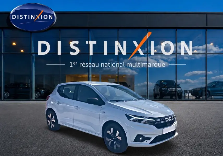 Vue 3/4 avant gauche d'une Dacia Sandero blanche 2025 avec jantes alu et vitres teintées devant un showroom Distinxion.