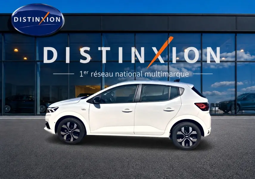 Profil droit d'une Dacia Sandero blanche 2025 garée devant une vitrine avec logo Distinxion.