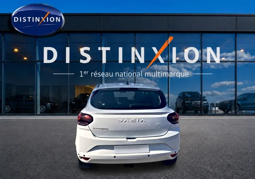 Vue arrière d'une Dacia Sandero blanche 2025 garée devant une vitrine avec logo Distinxion.