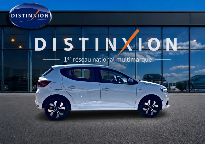 Profil côté gauche d'une Dacia Sandero blanche 2025 stationnée devant une vitrine Distinxion.