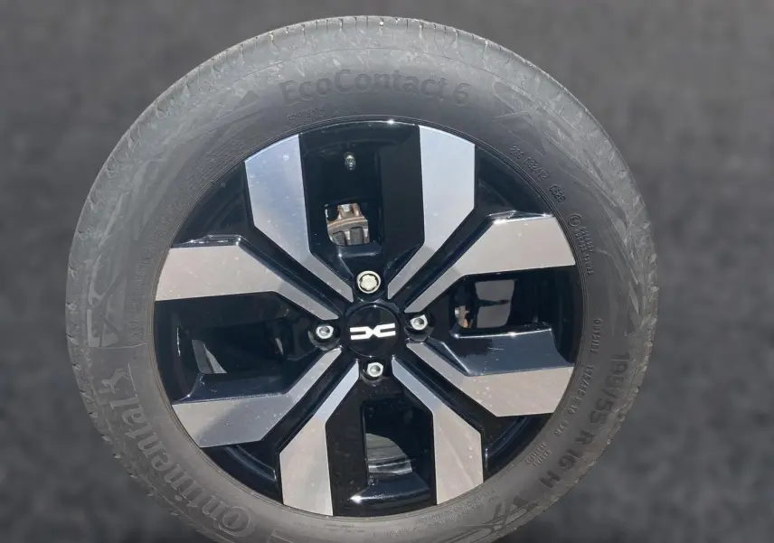 Gros plan sur la jante alu noire et argentée d'une Dacia Sandero blanche, mettant en valeur le logo central.