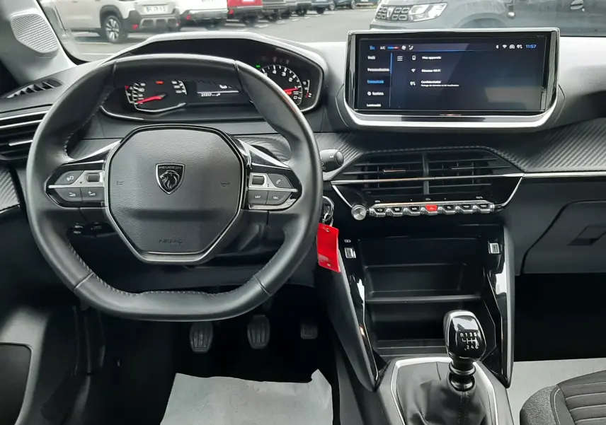 Vue intérieure avant de la Peugeot 208 2024, tableau de bord noir avec volant compact et écran tactile central.