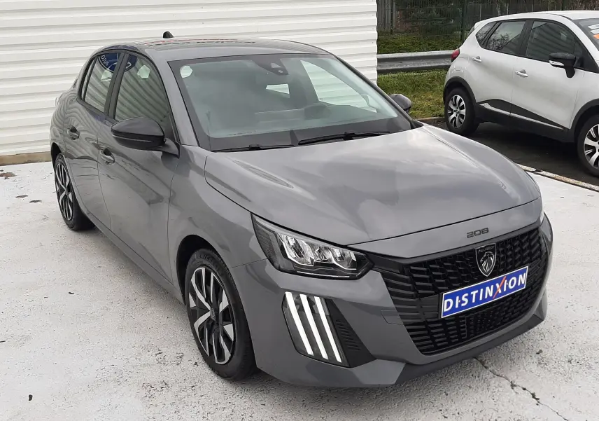Peugeot 208 gris sélénium vue 3/4 avant droit, avec calandre noire et feux LED distinctifs allumés.