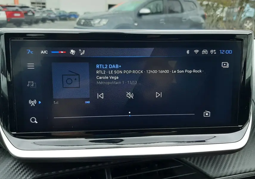 Vue rapprochée de l'écran tactile central du tableau de bord de la Peugeot 208 2024, affichant la radio DAB+ sur fond noir.