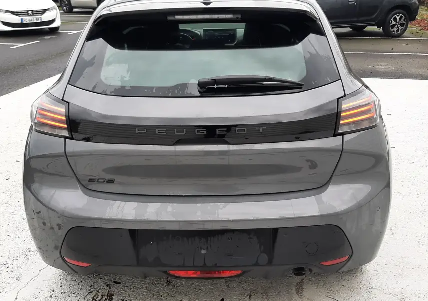 Vue arrière d'une Peugeot 208 gris selenium 2024 avec feux LED allumés et hayon fermé sur parking.