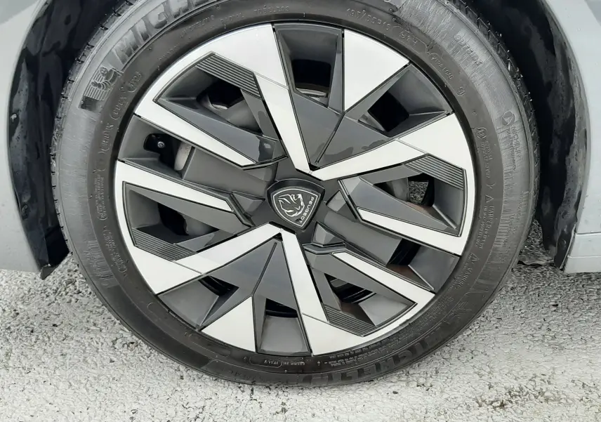 Gros plan sur la roue avant droite d'une Peugeot 208 2024 gris selenium avec jante alliage au design géométrique noir et argent.