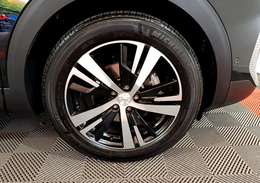Gros plan sur la roue avant droite noire du Peugeot 3008 2023 avec jante alliage bicolore et pneu Michelin.