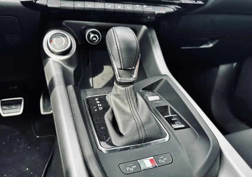 Gros plan sur la console centrale de l'Alfa Romeo Tonale 2024, avec levier de vitesse automatique et bouton de stationnement électrique.
