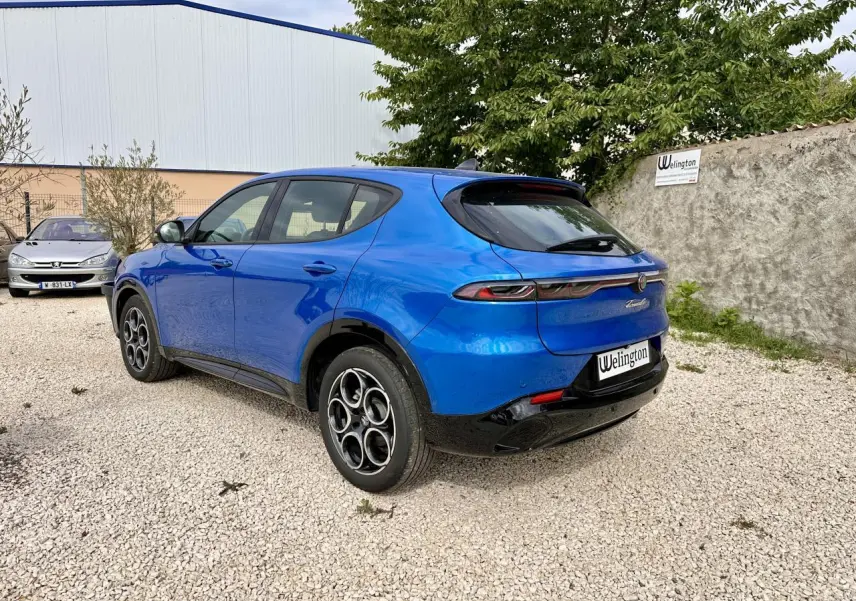 Vue 3/4 arrière droite d'une Alfa Romeo Tonale bleu métallisé avec jantes distinctives et feux arrière fins.