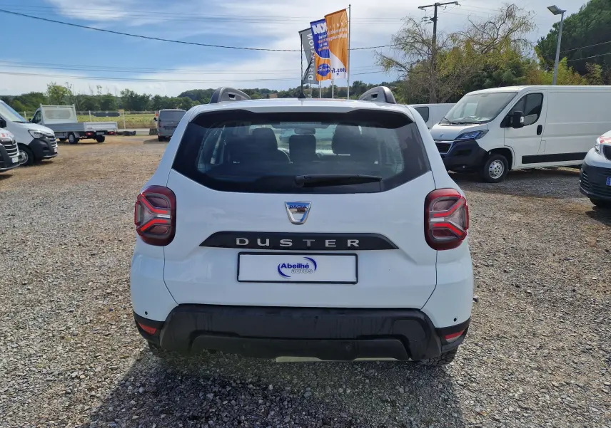 Vue arrière d’un Dacia Duster blanc 2022 avec feux arrière caractéristiques et logo DUSTER bien visible.
