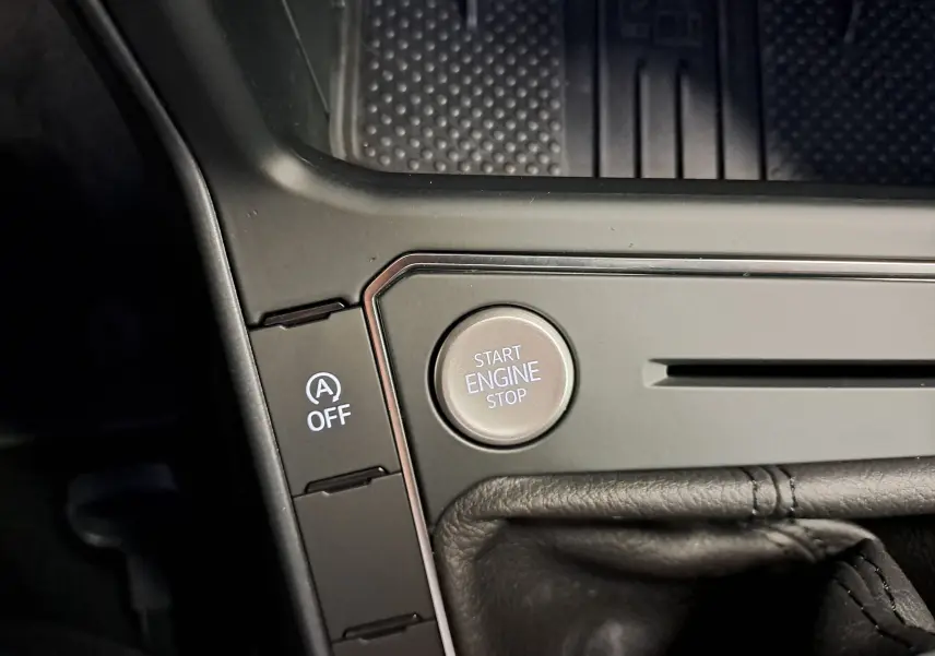 Gros plan sur le bouton Start Engine Stop et la commande Auto Start-Stop désactivée dans l’habitacle noir du Volkswagen Taigo.