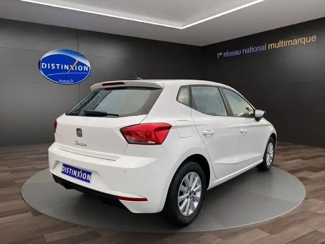 Vue 3/4 arrière droite d'une SEAT Ibiza 1.0 MPI 80 STYLE blanche Candy en showroom avec jantes alliage et feux LED.