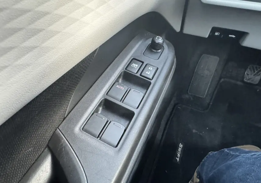 Gros plan sur les commandes de lève-vitres et rétroviseurs côté conducteur d'une Suzuki Swift blanche 2025.