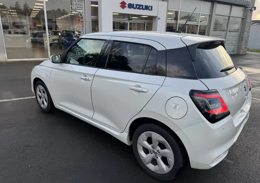 Suzuki Swift 1.2 Privilege blanc vue 3/4 arrière droit, avec vitres teintées et jantes alliage spécifiques.