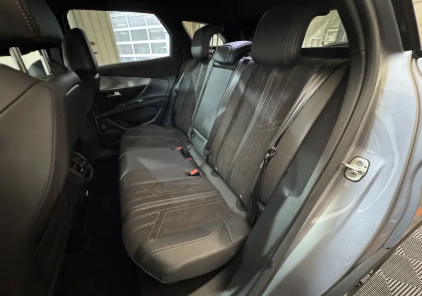 Vue intérieure côté arrière droit du Peugeot 3008 gris clair, montrant la banquette arrière en cuir noir avec surpiqûres contrastées.
