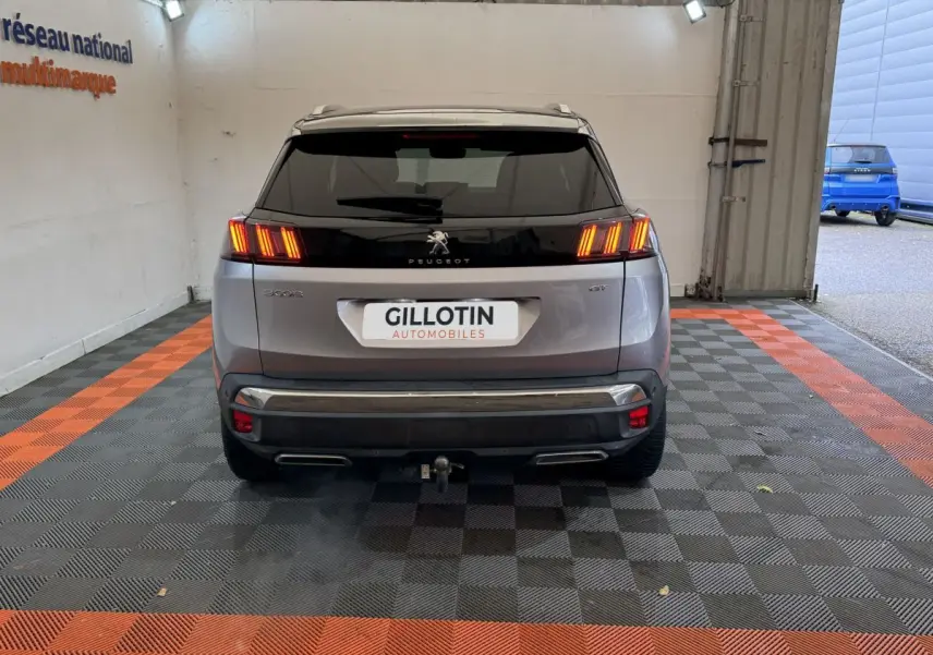 Vue arrière d'un Peugeot 3008 GT gris clair avec feux LED allumés et attelage visible en intérieur showroom.