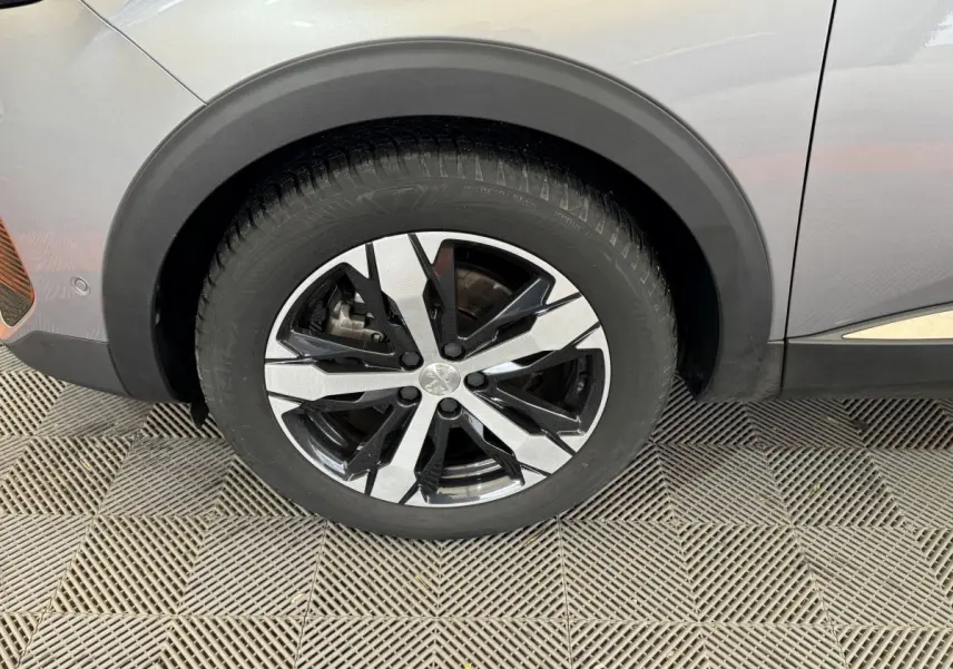 Gros plan sur la roue avant gauche du Peugeot 3008 gris clair, mettant en valeur la jante alliage bicolore au design moderne.