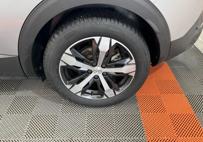 Gros plan sur la roue avant gauche d’un Peugeot 3008 gris clair avec jante alliage bicolore moderne.