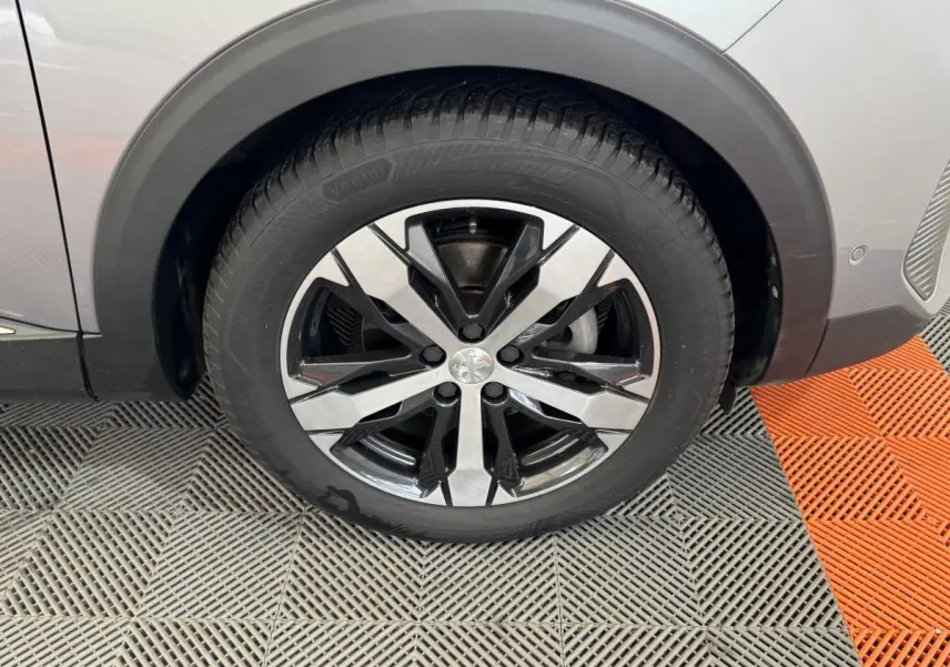 Gros plan sur la roue avant gauche du Peugeot 3008 gris clair avec jante alliage bicolore et logo Peugeot au centre.