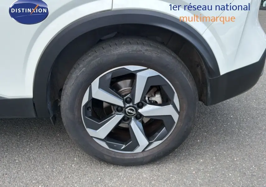 Gros plan sur la roue arrière droite du Nissan Qashqai blanc nacré, mettant en valeur la jante alliage bicolore au design moderne.