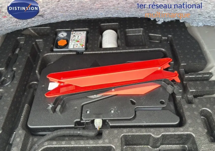 Gros plan sur le rangement sous coffre avec triangle de signalisation rouge et kit de réparation sur Nissan Qashqai blanc nacré.