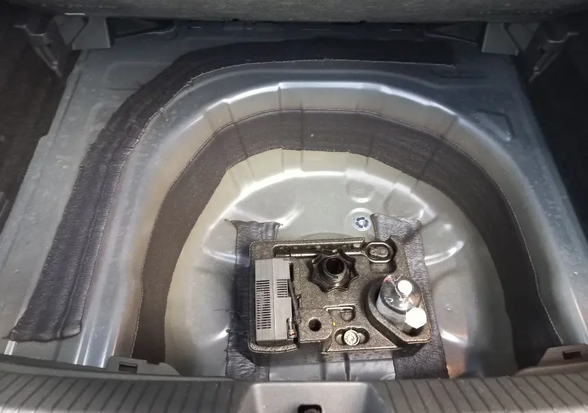 Vue rapprochée du coffre du Volkswagen Taigo 2025 montrant le logement de la roue de secours vide et ses accessoires.