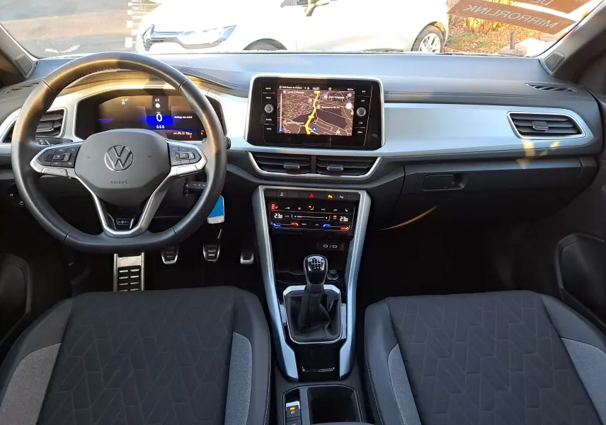 Vue intérieure avant du Volkswagen T-Roc gris Ascot 2025, avec tableau de bord numérique et boîte manuelle visible.