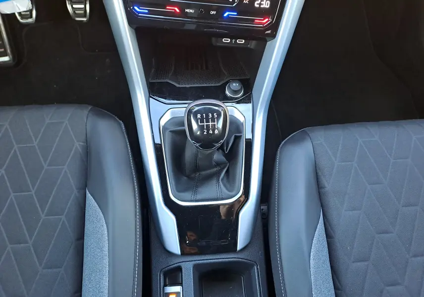 Vue plongeante sur la console centrale du Volkswagen T-Roc gris Ascot, avec levier de vitesses manuel et sièges tissu noir.