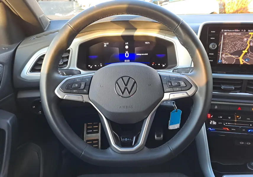 Vue intérieure centrée sur le volant noir du Volkswagen T-Roc 2025 avec tableau de bord digital et écran de navigation.