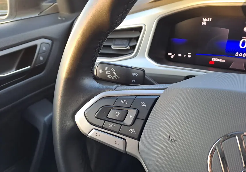 Gros plan sur le volant noir du Volkswagen T-Roc 2025 avec commandes intégrées et tableau de bord numérique en arrière-plan.