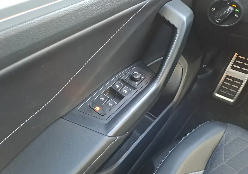 Vue intérieure côté conducteur du Volkswagen T-Roc 2025, avec commandes de vitres et rétroviseurs, garniture noire et surpiqûres blanches.