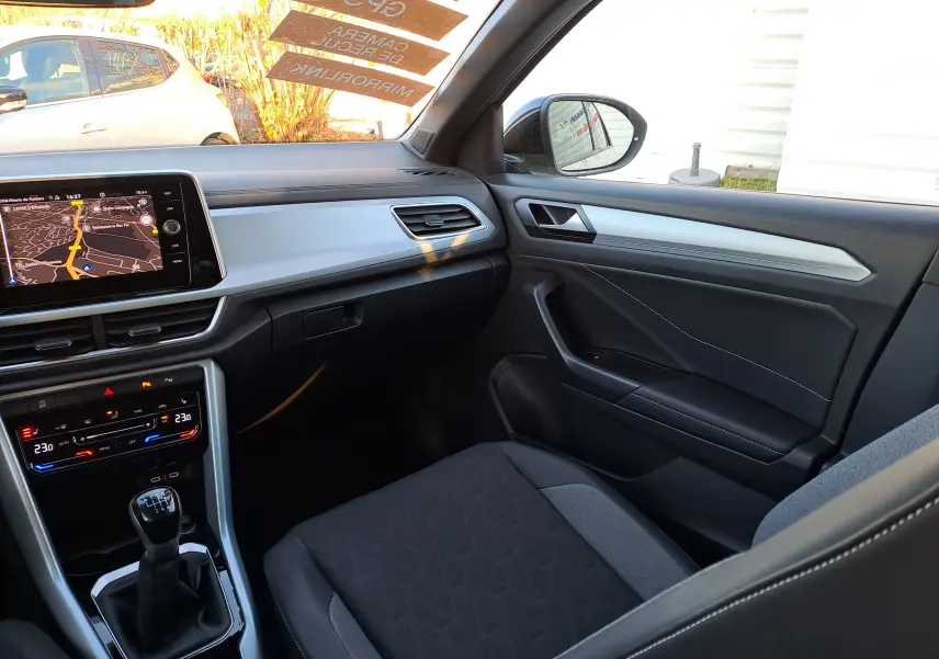 Vue intérieure côté passager du Volkswagen T-Roc 2025 gris Ascot, mettant en valeur la console centrale et la boîte manuelle.