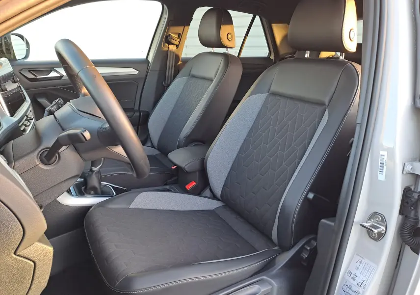 Vue intérieure côté conducteur du Volkswagen T-Roc 2025 avec sièges tissu et cuir gris, volant et tableau de bord visibles.