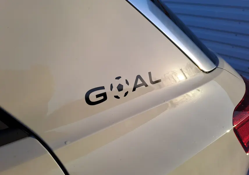 Gros plan sur le coffre gris ascot d'un Volkswagen T-Roc 2025 avec l'inscription noire "GOAL" et partie du feu arrière droit.