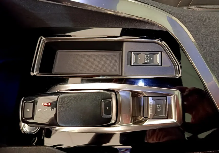 Gros plan sur la console centrale noire brillante du Peugeot 3008 rouge, avec levier de vitesses automatique et bouton Drive Mode.