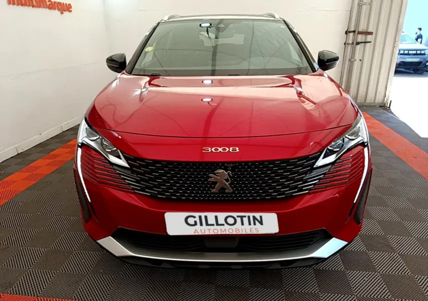 Vue frontale d'un Peugeot 3008 rouge avec calandre noire et logo lion au centre, en intérieur showroom.