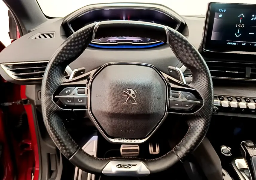 Vue rapprochée du volant cuir noir GT du Peugeot 3008 rouge 2021 avec tableau de bord digital et écran tactile.