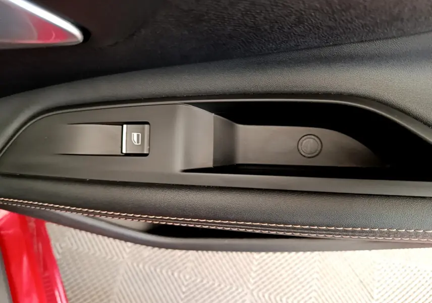 Gros plan sur la commande de lève-vitre côté gauche d'une Peugeot 3008 GT rouge avec surpiqûres contrastées.