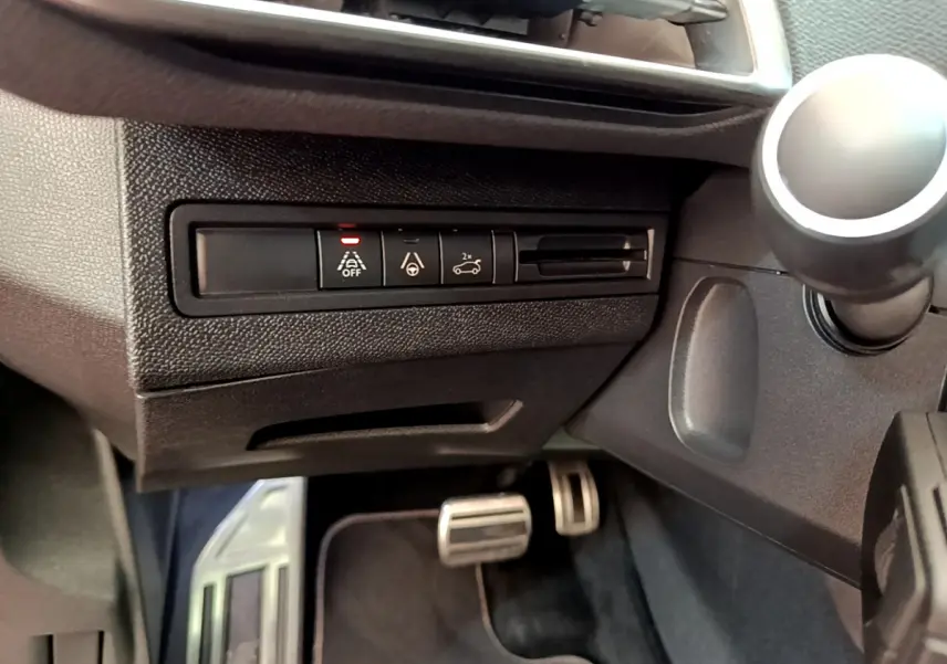 Vue rapprochée des commandes d'assistance à la conduite sur le côté gauche du tableau de bord noir du Peugeot 3008 rouge.