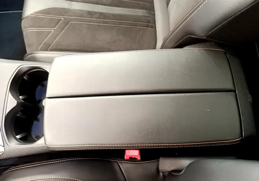 Vue rapprochée de l'accoudoir central noir avec surpiqûres orange et porte-gobelets du Peugeot 3008 GT rouge 2021.