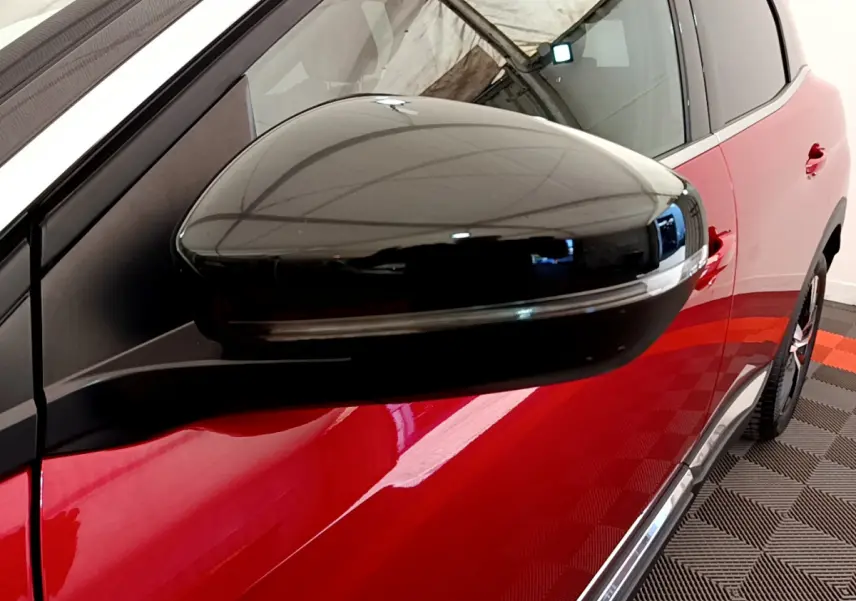 Gros plan sur le rétroviseur noir du côté gauche d'un Peugeot 3008 rouge brillant, vue latérale partielle.
