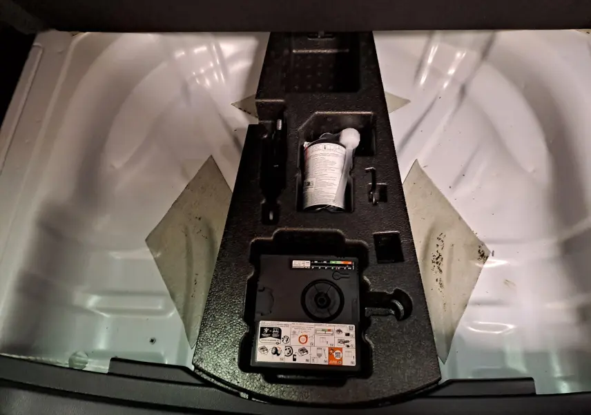 Vue plongeante sur le coffre d’un Skoda Karoq 2025 blanc lune, montrant le rangement sous le plancher avec kit de réparation.