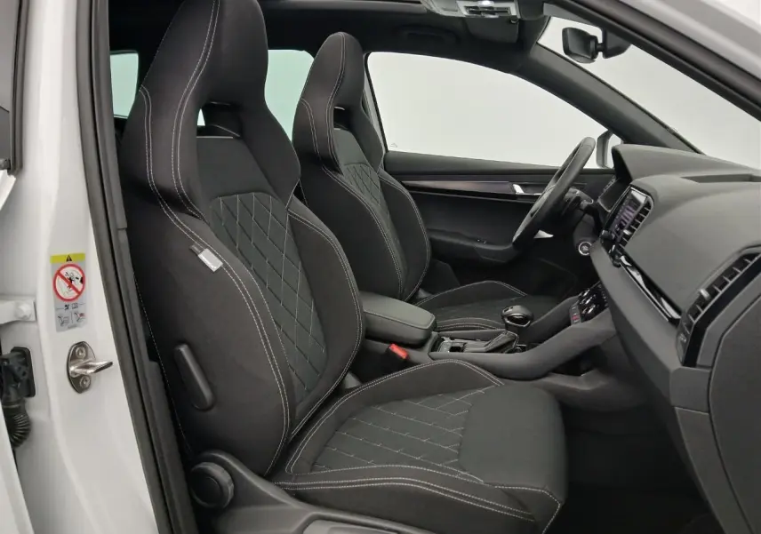 Intérieur du Skoda Karoq 2025 blanc lune, vue côté gauche sur les sièges sport noirs avec surpiqûres blanches.