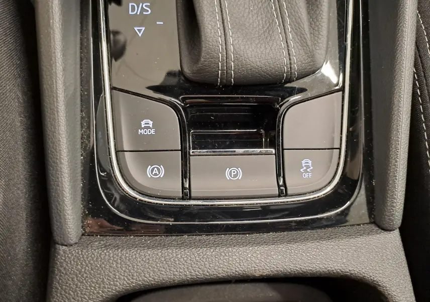 Gros plan sur la console centrale noire brillante du Skoda Karoq 1.5 TSI 150 DSG7 Sportline avec boutons de mode et frein à main électronique.