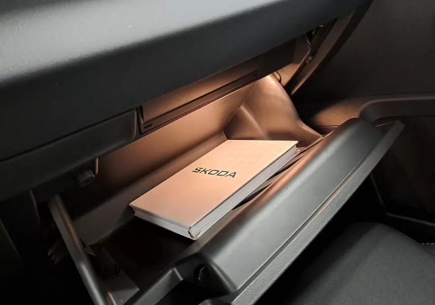 Vue intérieure du vide-poche passager ouvert d'un Skoda Karoq blanc lune 2025 avec manuel de bord visible.
