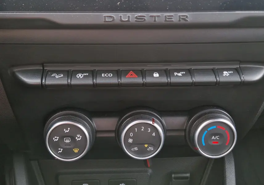 Gros plan sur la console centrale du Dacia Duster 2023 blanc, montrant les commandes de climatisation et les boutons de fonction.